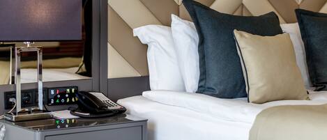 Habitación de hotel con cama, mesita de noche con teléfono y lámpara, y pared con diseño geométrico.