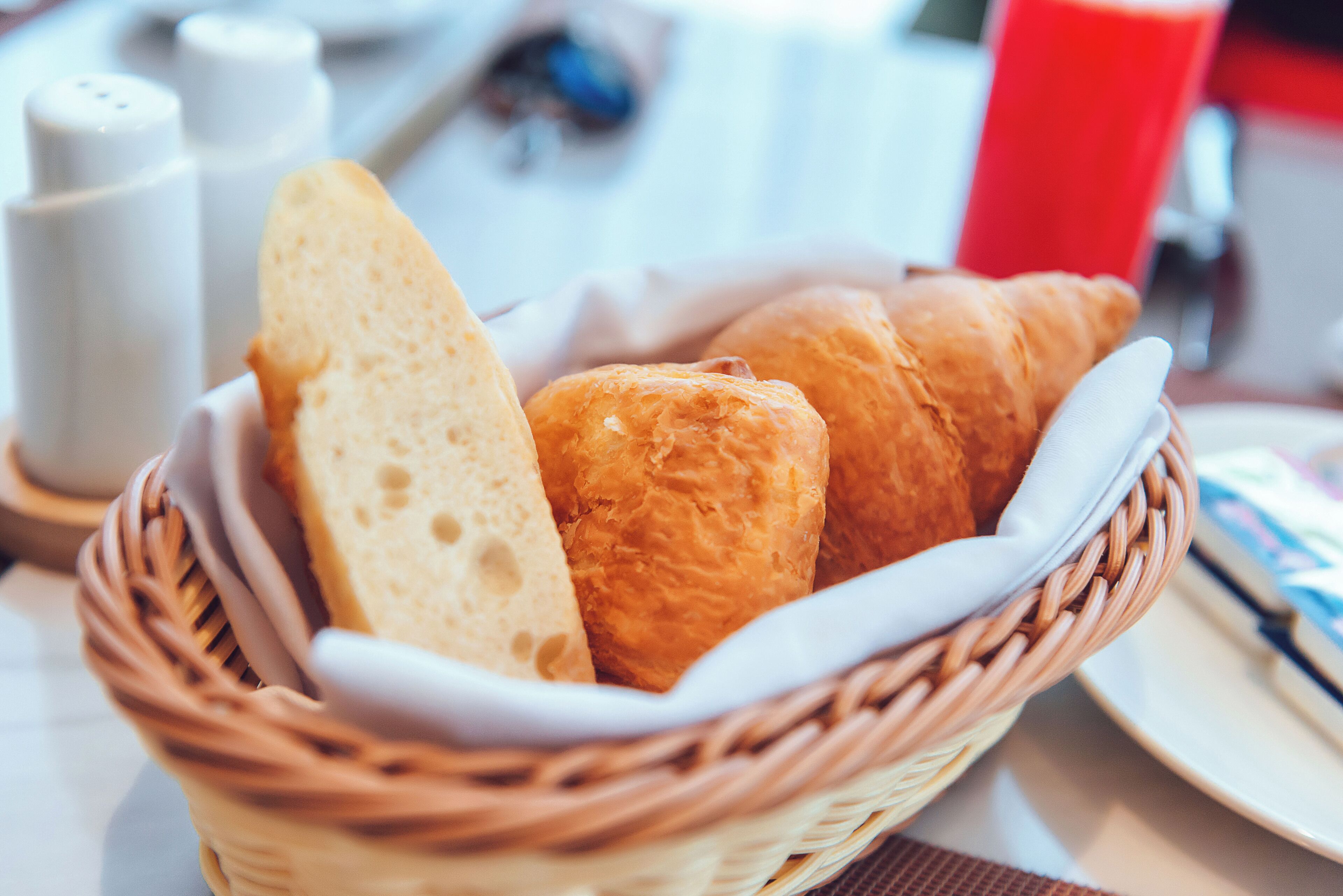 En korg med frallor och en baguette på ett bord.