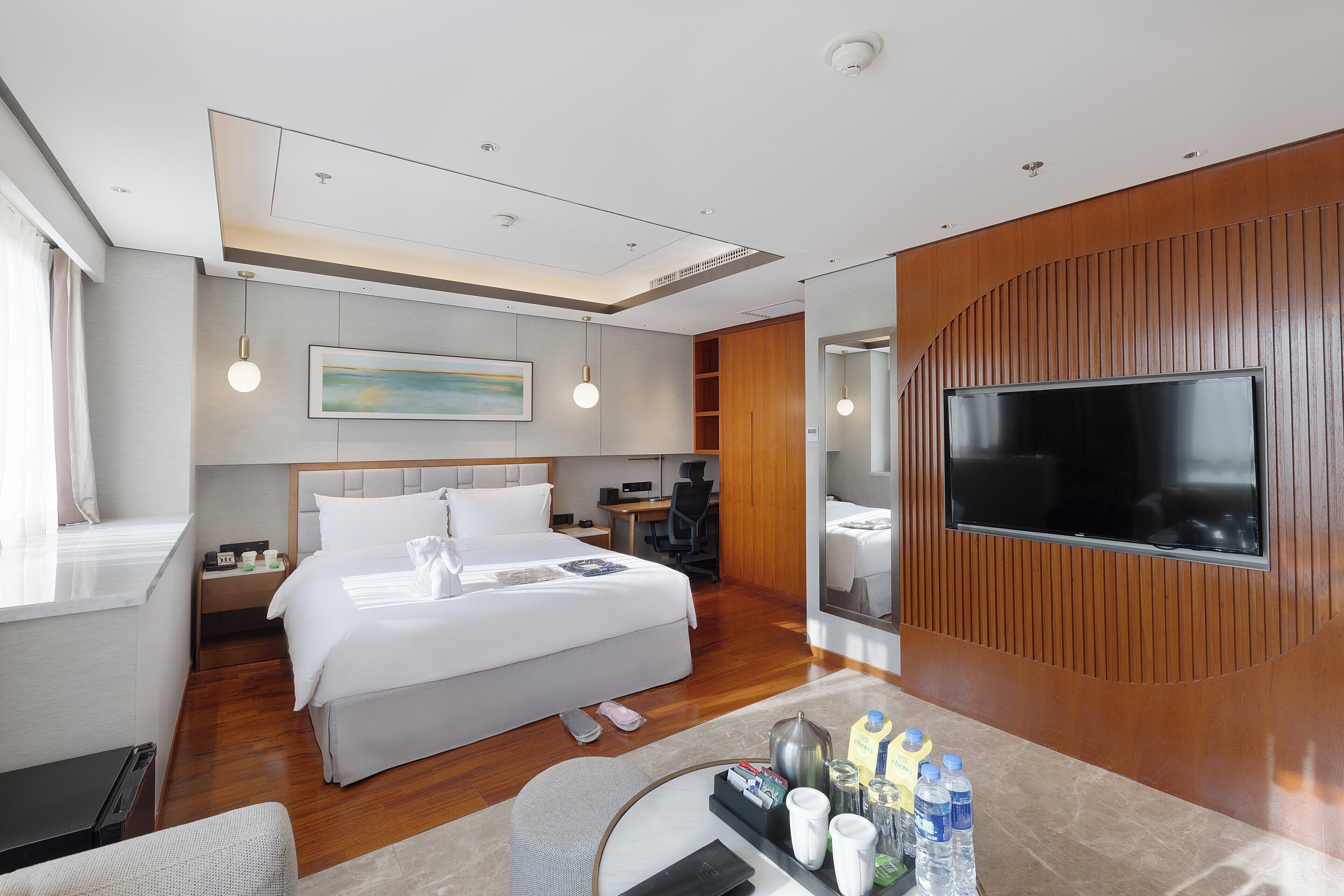 A modern hotel room with a large bed, a desk, a flat-screen TV, and a dining area.