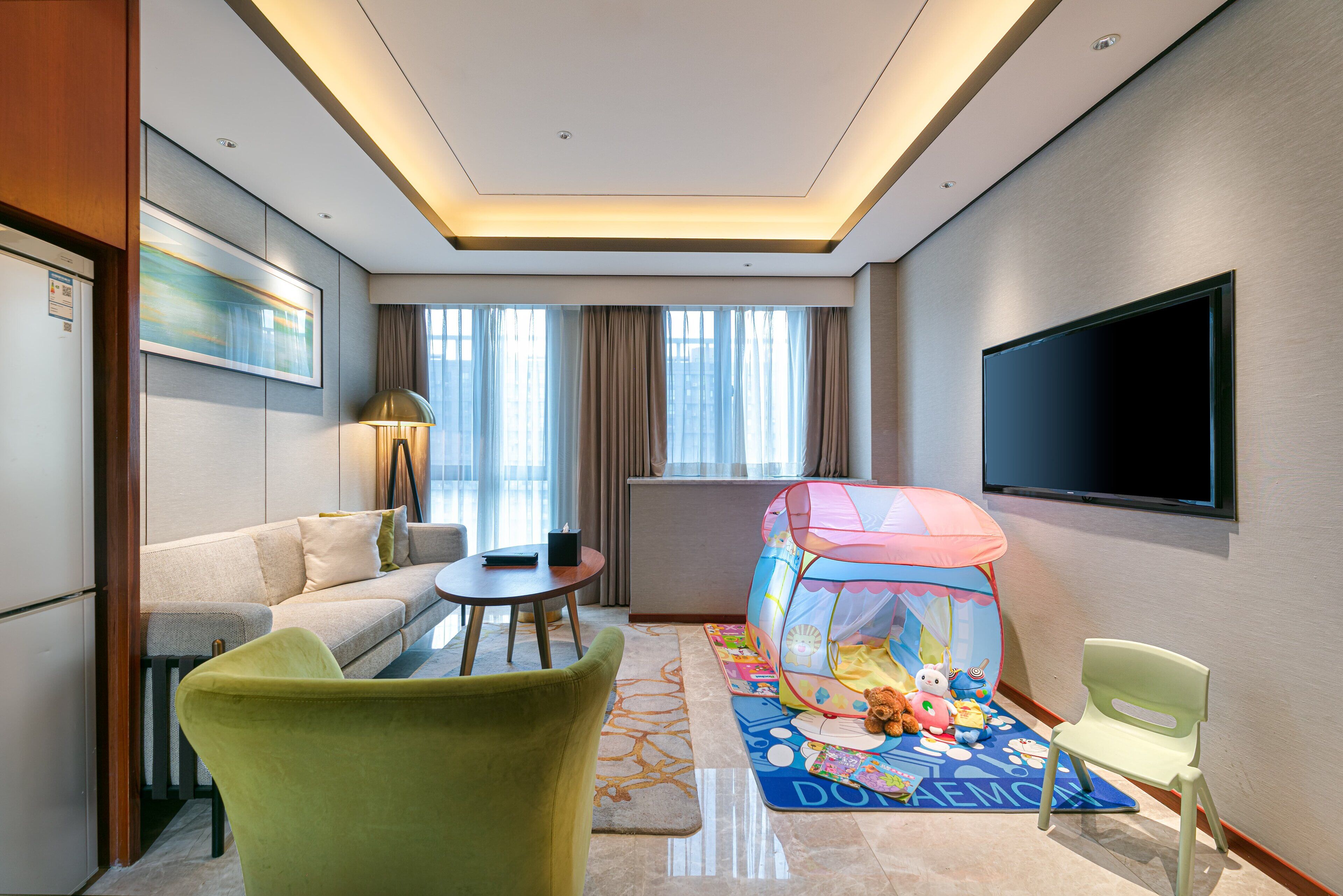 A hotel room with a sofa, a small table, a TV, a children's play tent, and a carpet with a cartoon character.