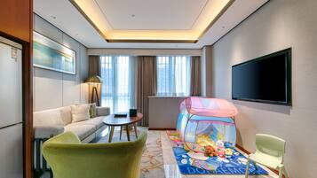 A hotel room with a sofa, a small table, a TV, a children's play tent, and a carpet with a cartoon character.
