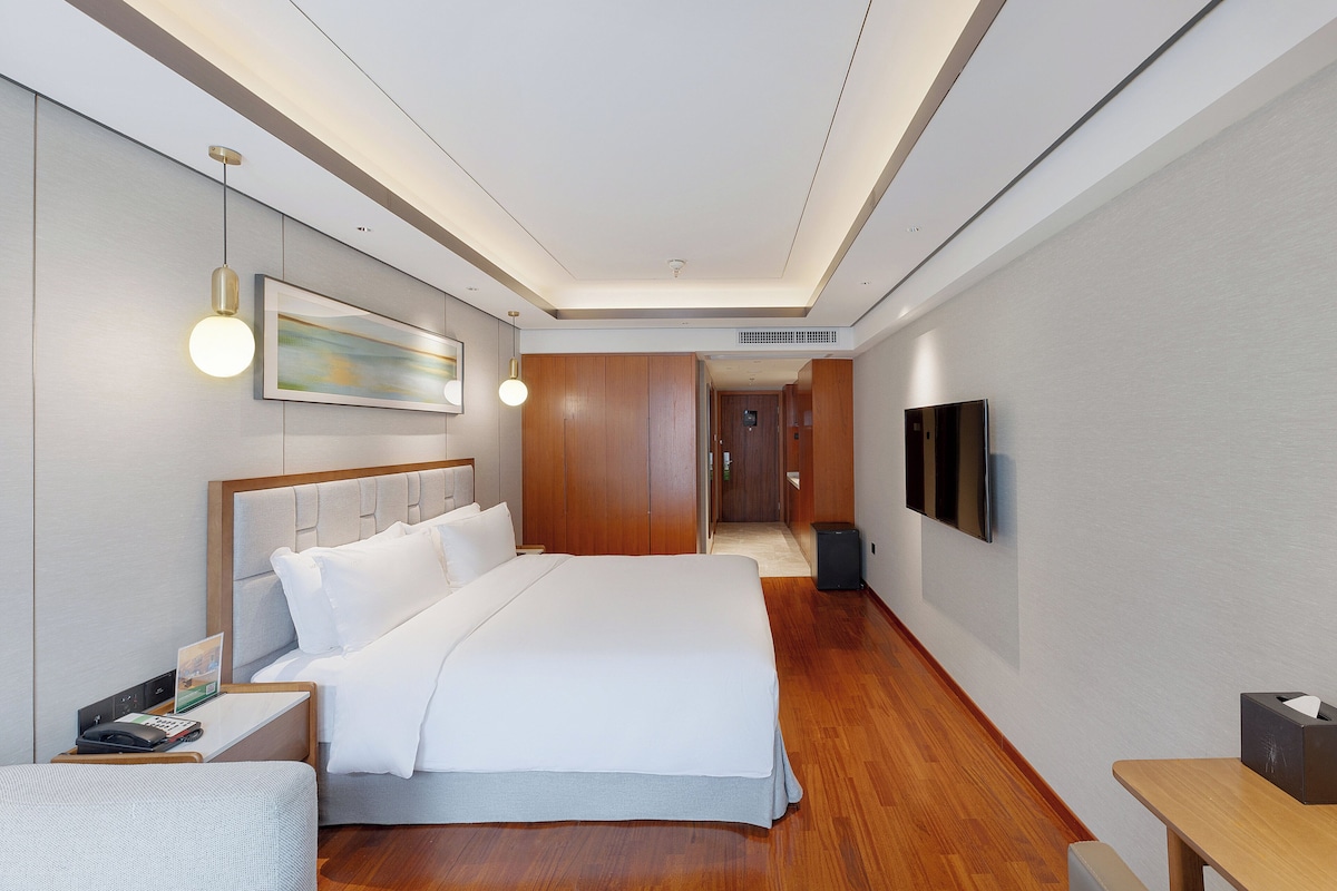 Een moderne hotelkamer met een groot bed, nachtkastjes, een flatscreen televisie en een houten vloer.