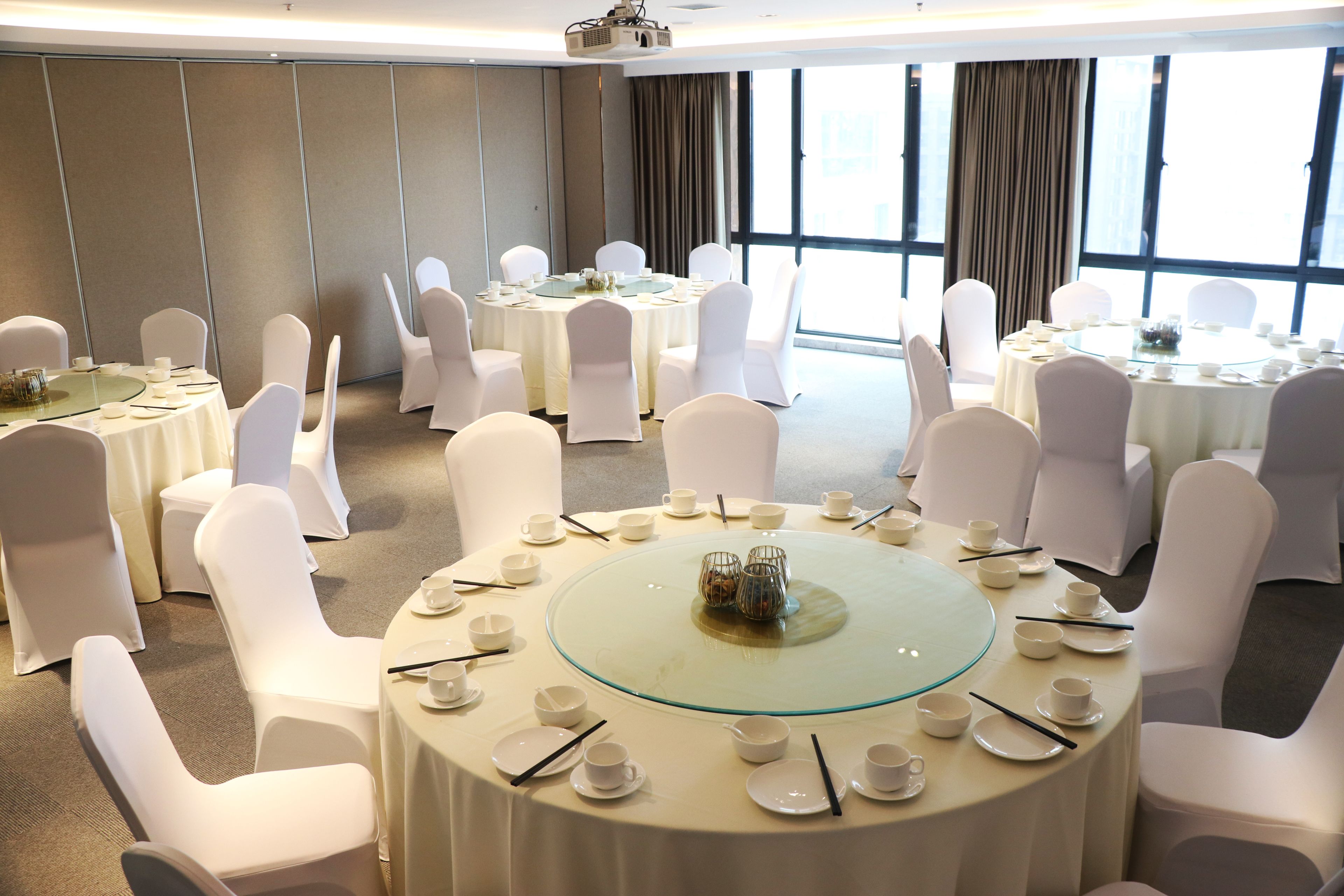 A conference room with multiple round tables, each set with white chairs and tableware.