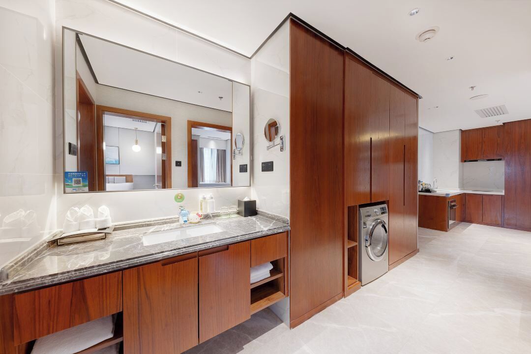 A modern bathroom with a large mirror, wooden cabinets, a built-in washing machine, and a marble countertop.