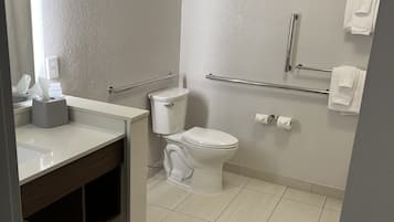 A modern bathroom with a toilet, sink, and handrails.