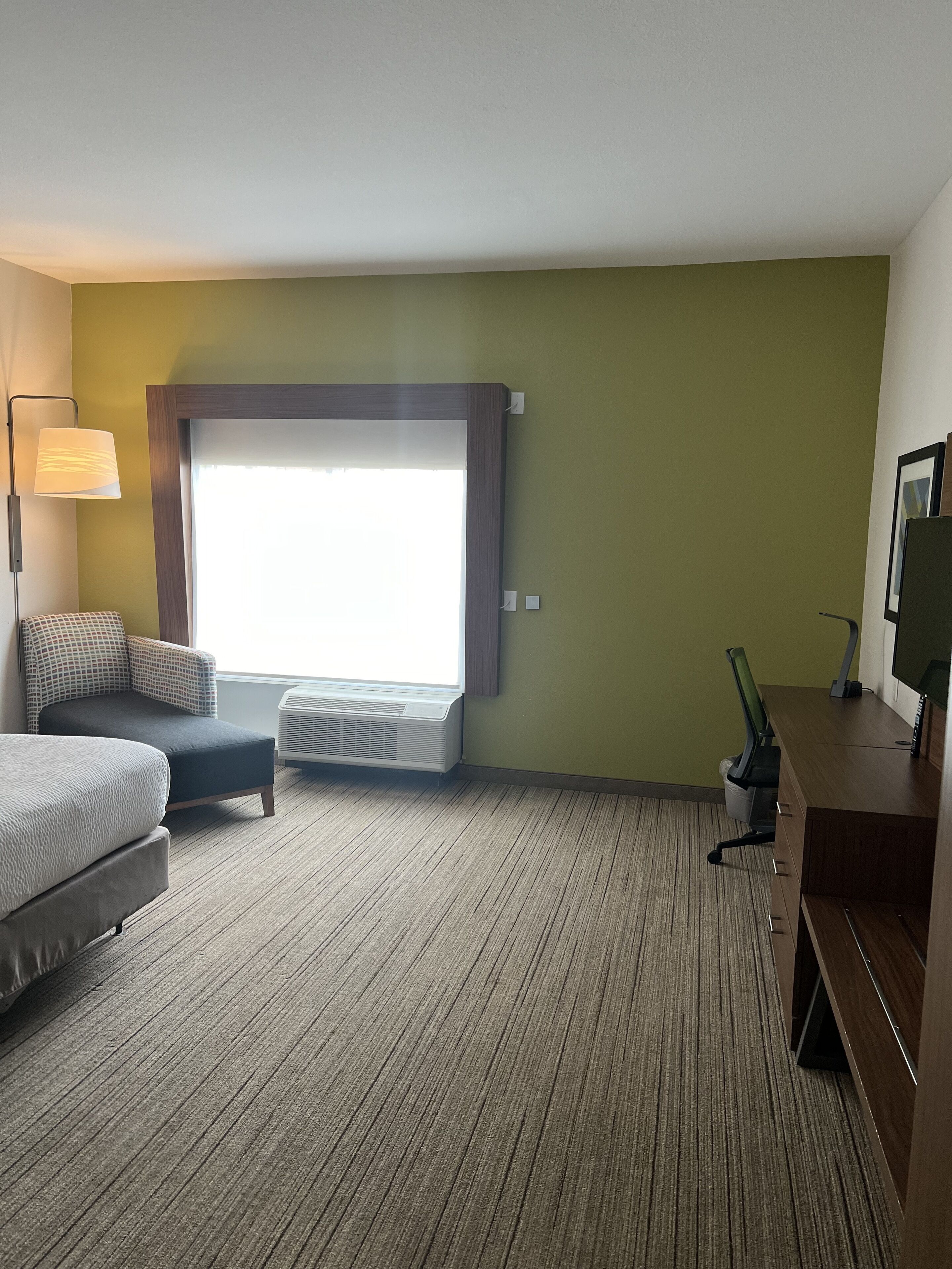 Une chambre d’hôtel équipée d’un lit, d’un bureau, d’une chaise, d’une lampe, d’une fenêtre et d’un climatiseur.