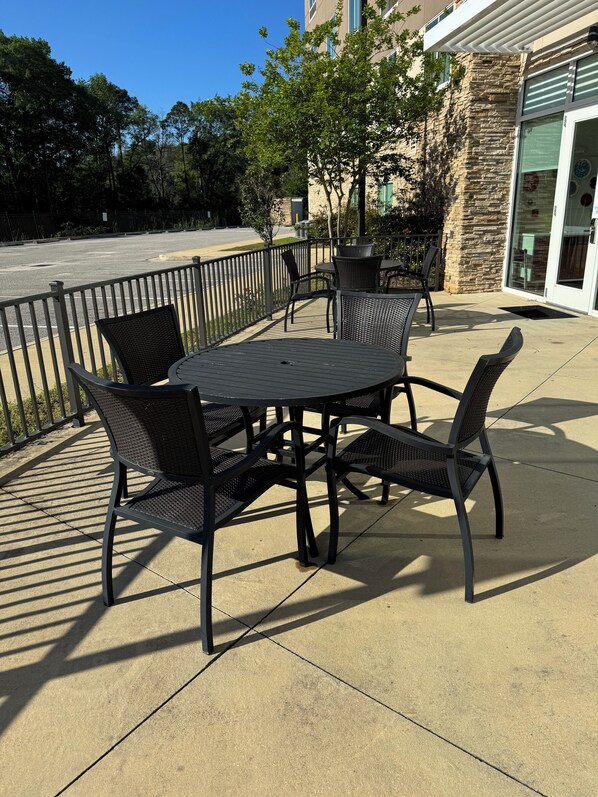 Une terrasse extérieure avec une table ronde et quatre chaises, un bâtiment en pierre en arrière-plan et un parking.