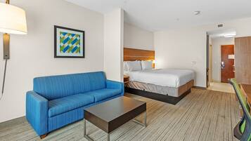 Quarto de hotel com um sofá azul, uma cama com roupa de cama branca, uma mesinha e um quadro na parede.