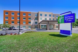 A Holiday Inn Express & Suites building with a modern design, featuring a mix of brick and stucco exteriors, and a clear blue sky.