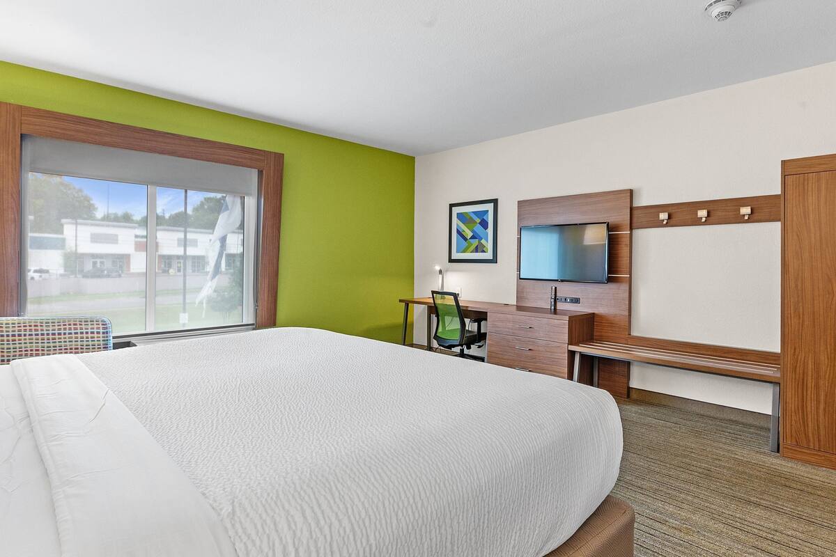 A hotel room with a large bed, a desk with a chair, a TV, and a wardrobe.