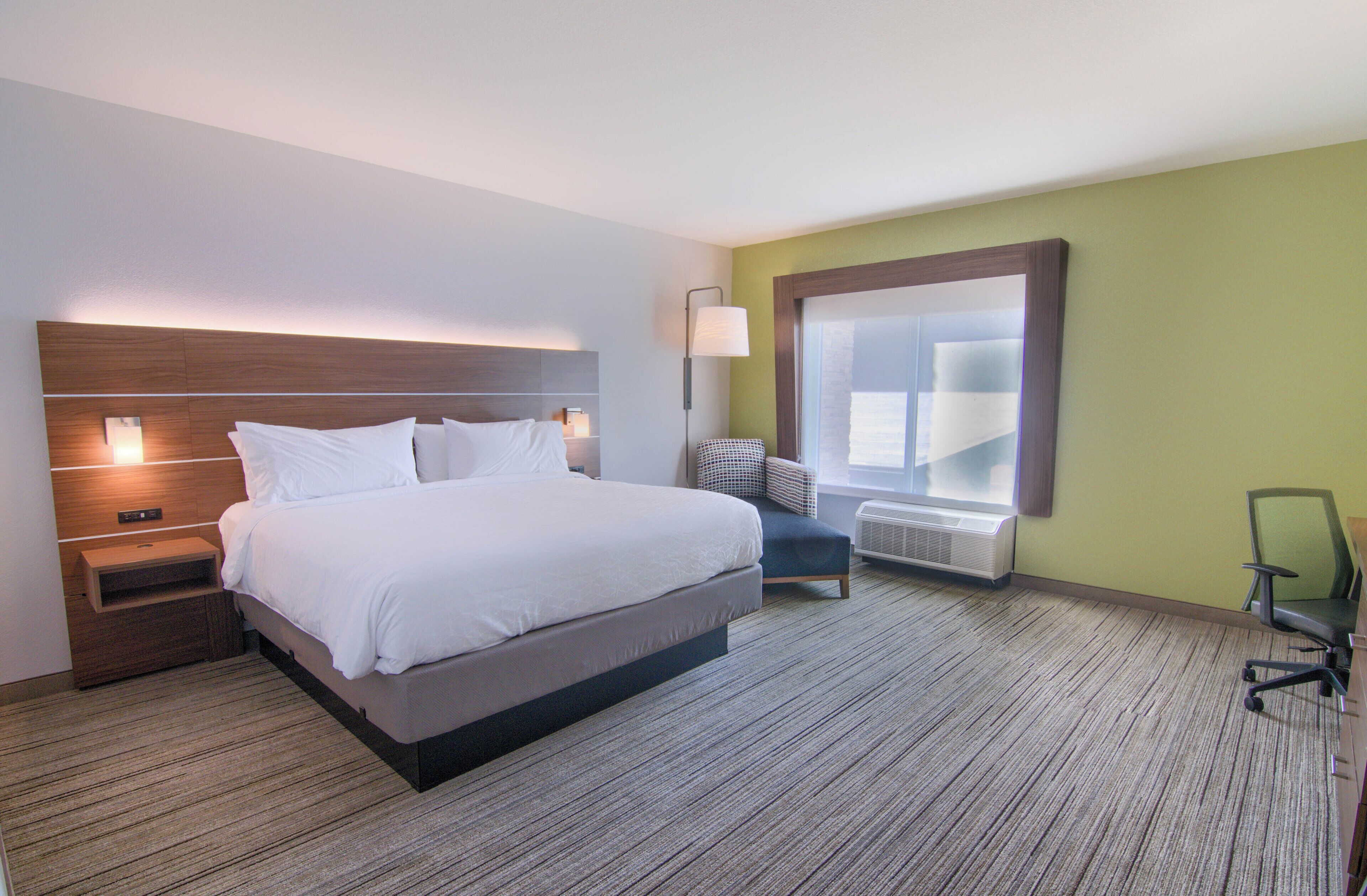 A hotel room with a large bed, bedside tables, a chair, a window, and a wall-mounted lamp.