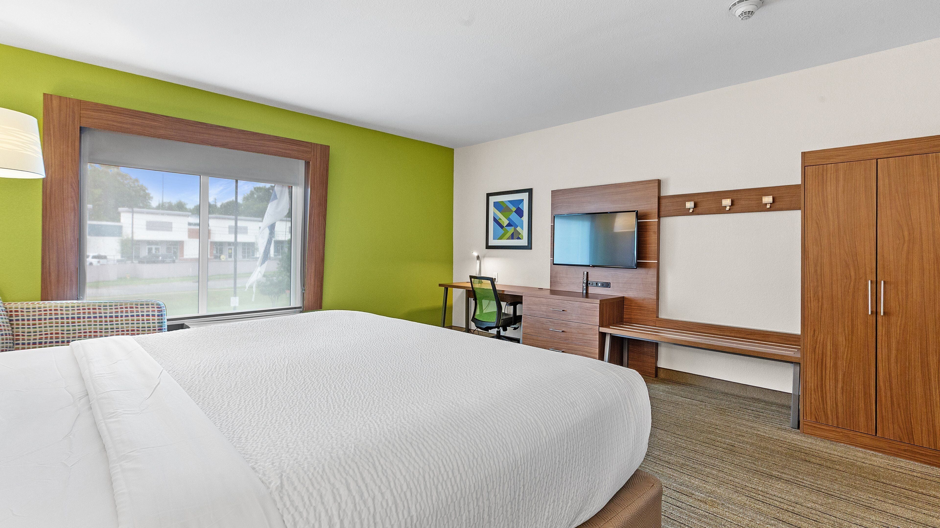 A hotel room with a large bed, a desk with a chair, a TV, and a wardrobe.