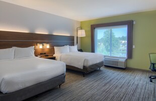 Una habitación de hotel con dos camas, una mesita de noche, una lámpara, un ventanal y un radiador.