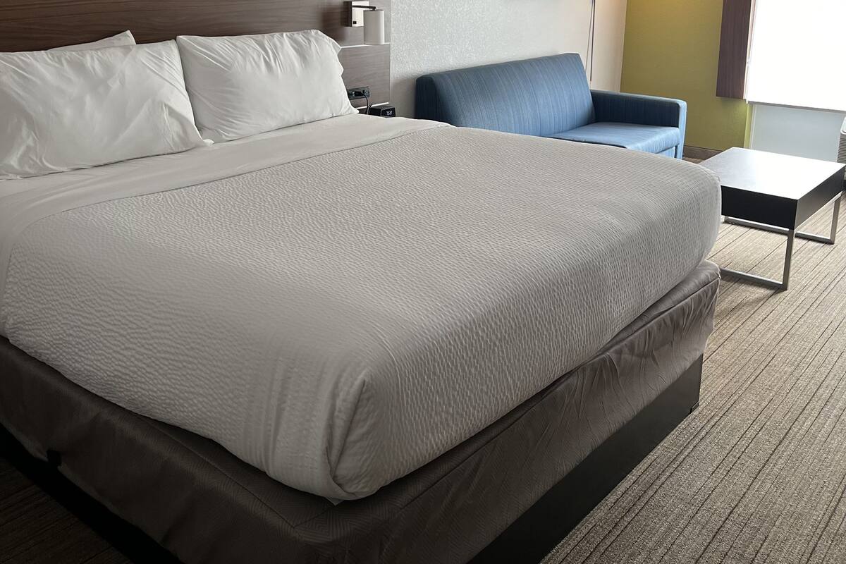 A hotel room with a large bed, a desk, a chair, and a lamp.