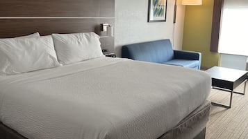 A hotel room with a large bed, a desk, a chair, and a lamp.