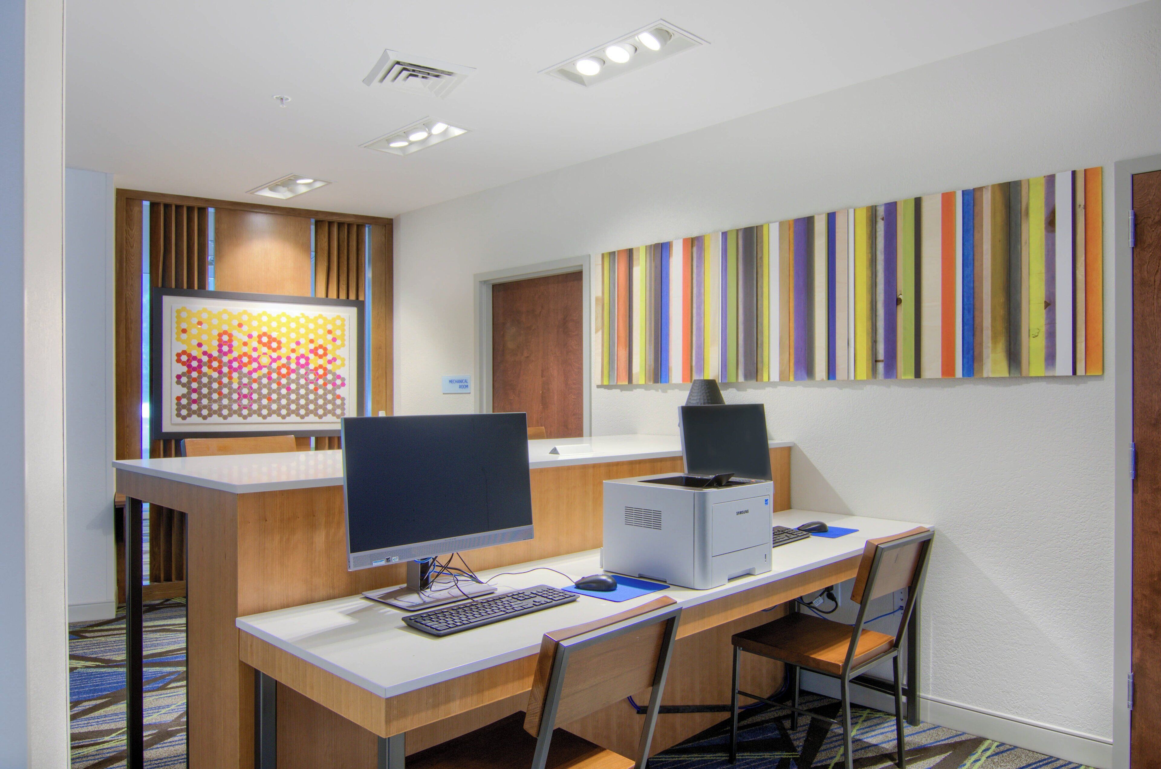 A modern office space with a desk, computer, and printer. There is a framed artwork on the wall and a sign indicating a mechanical room.