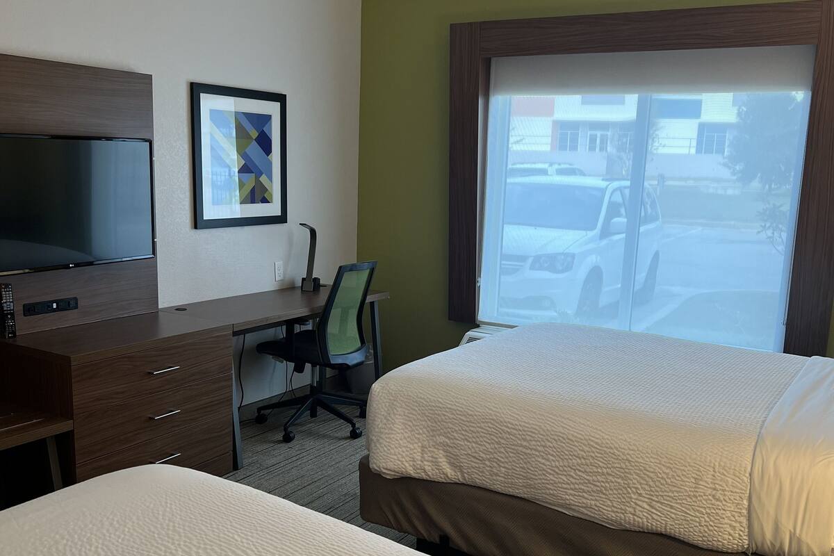 A hotel room with two beds, a desk with a TV, a chair, and a window with a view of a parking lot.
