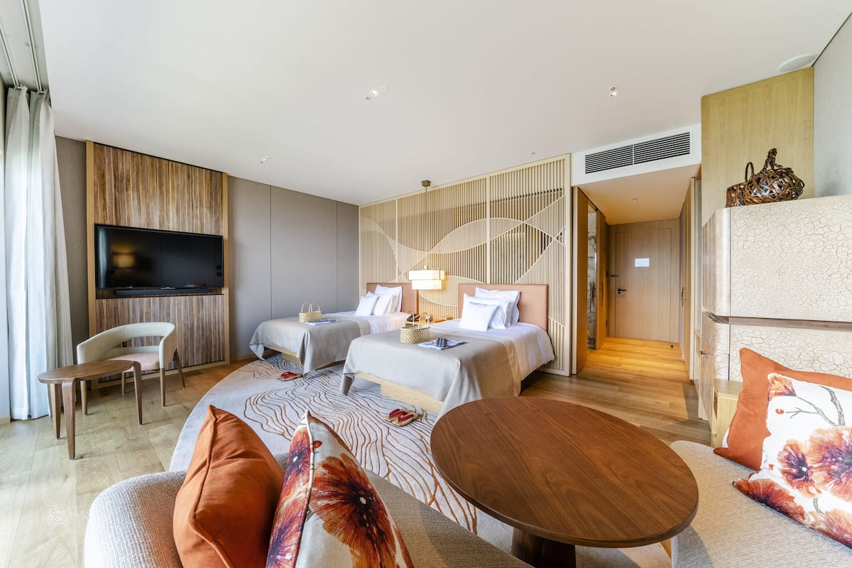 A modern hotel room with two beds, a TV, a dining table, and a sofa.