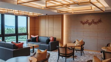 Un espacio lounge moderno con sofá, sillones y mesas, que cuenta con ventanas amplias y una pared de madera con un adorno decorativo.