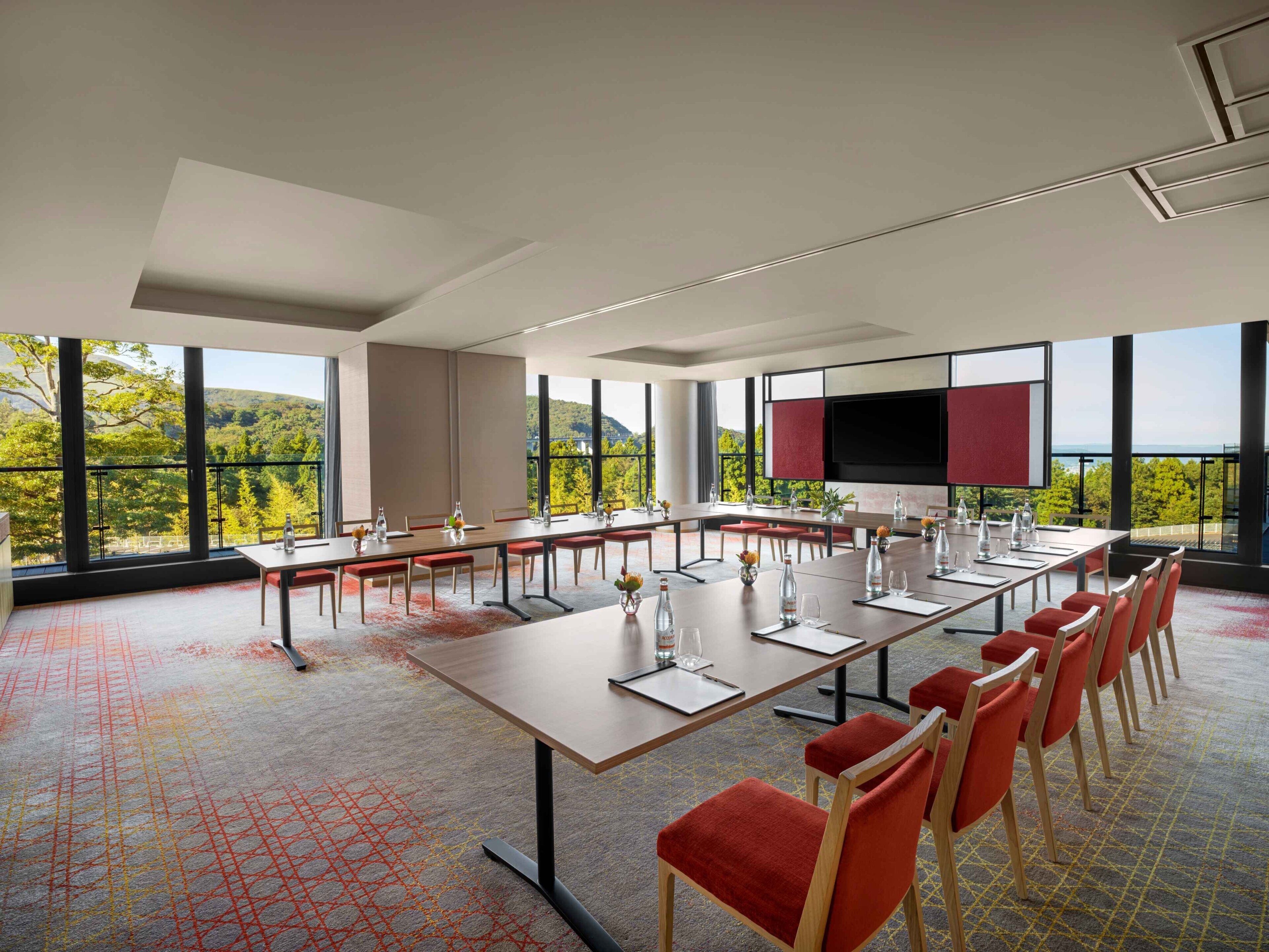 Ein Konferenzraum mit einem langen Tisch, Stühlen und einem großen Fenster mit Blick auf Grünflächen.