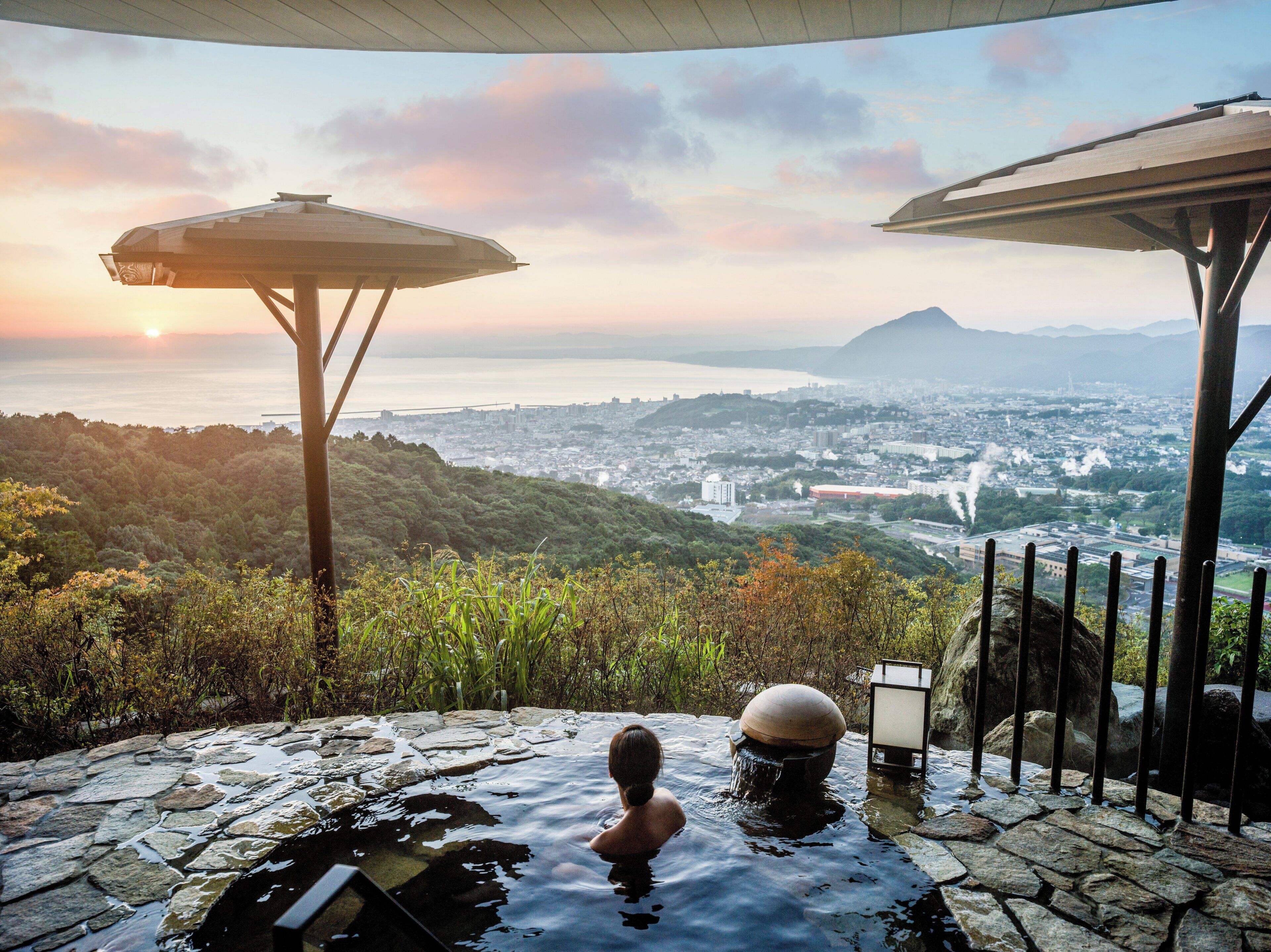 A person in a hot spring with a view of a cityscape and mountains.