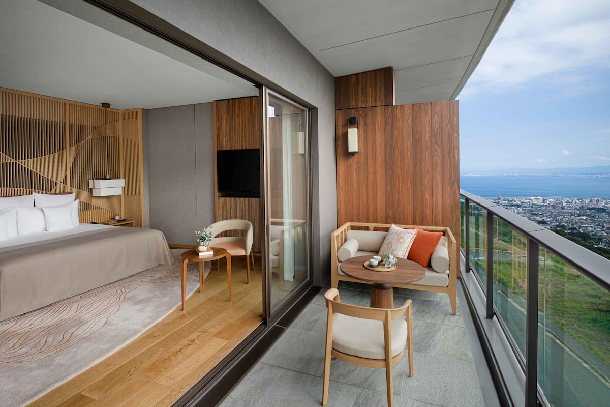 A modern hotel room with a balcony, a bed, a sofa, and a dining table.