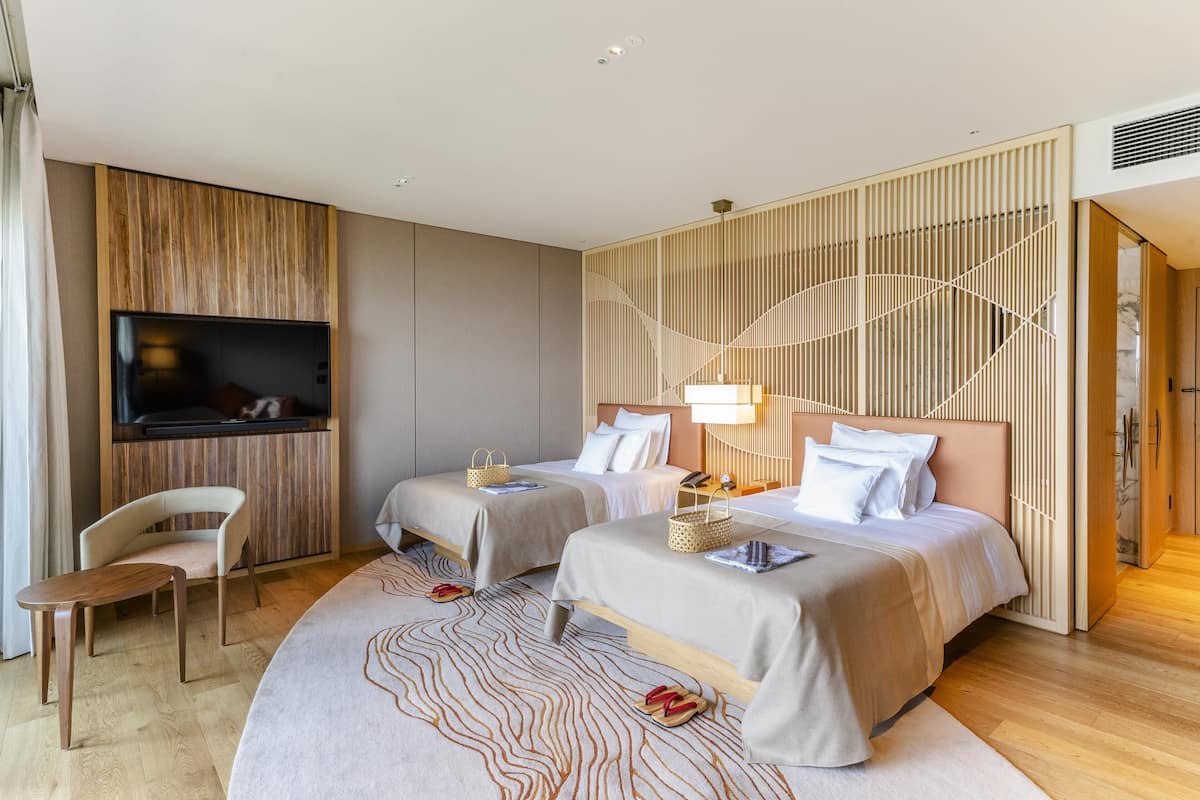 A modern hotel room with two beds, a TV, a desk, and a chair.