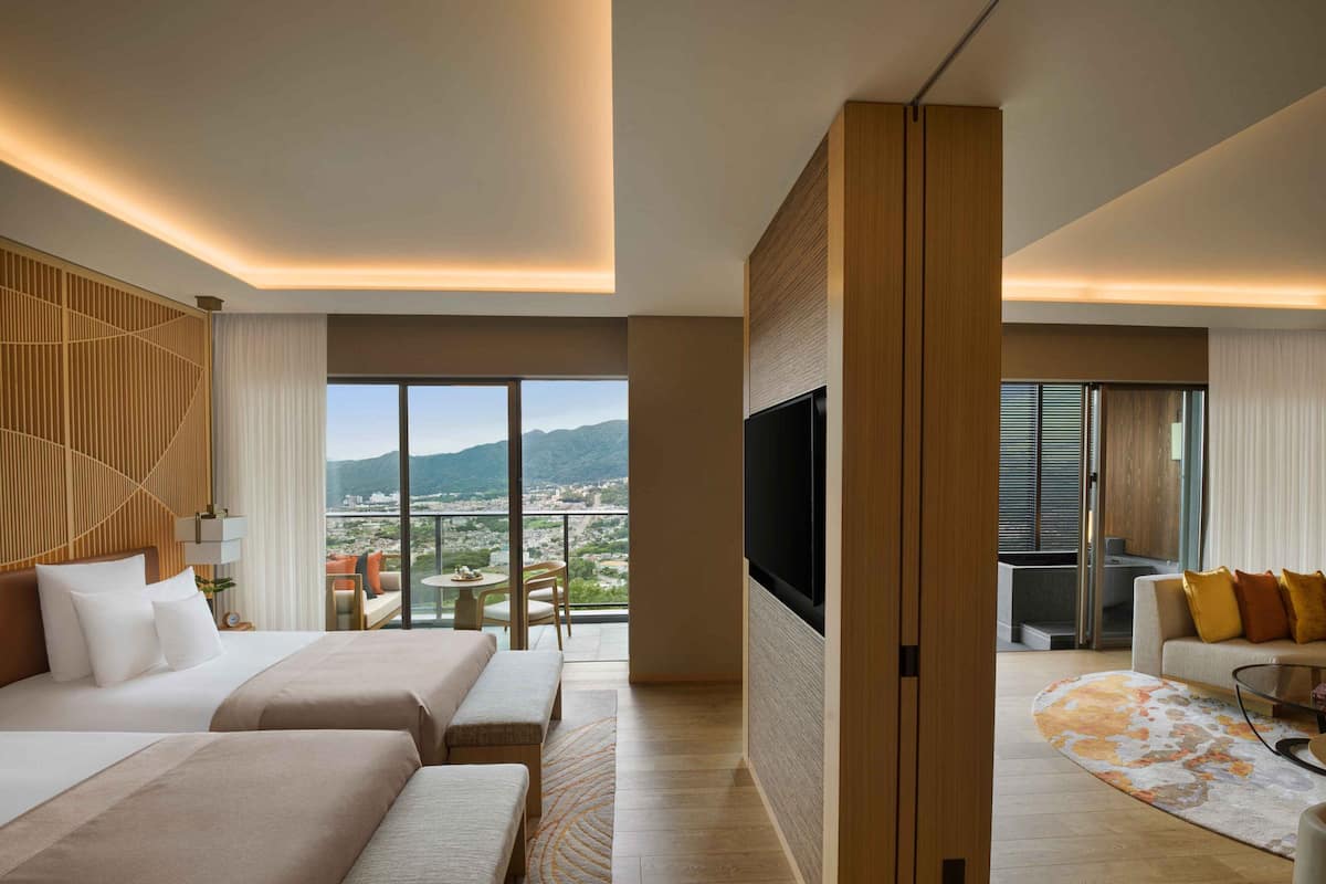 A hotel room with a large bed, a TV, and a balcony with a city view.