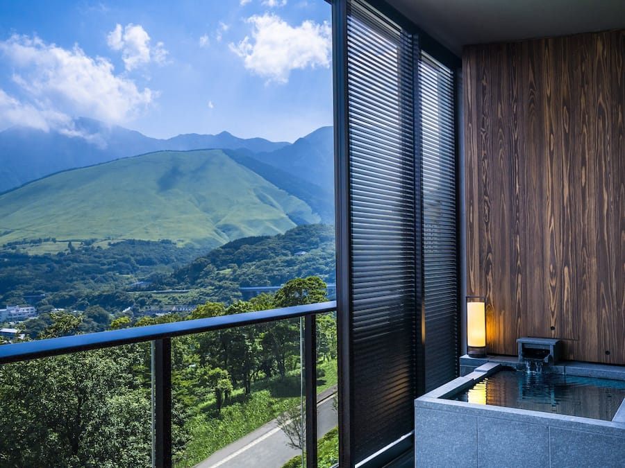 Un balcón con vista a una cadena montañosa, una pared de madera y un pequeño elemento acuático.