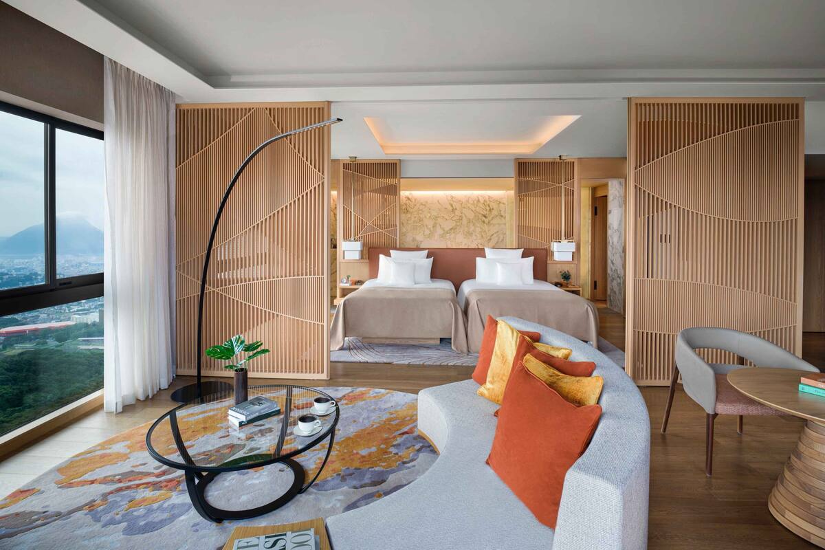 A modern hotel room with a large bed, a sofa, a dining table, and a view of the city.