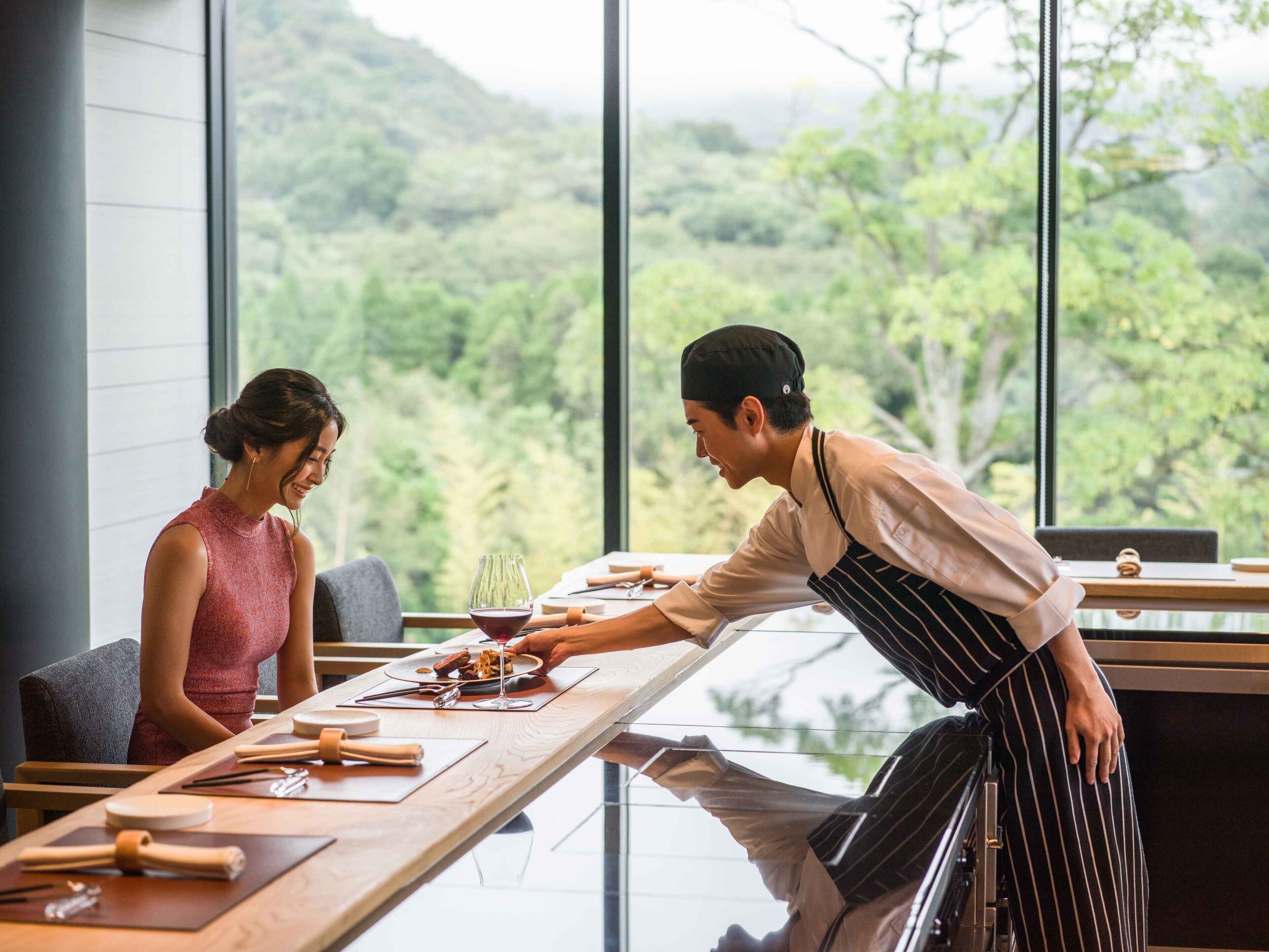 A restaurant with a large window overlooking a forested area.