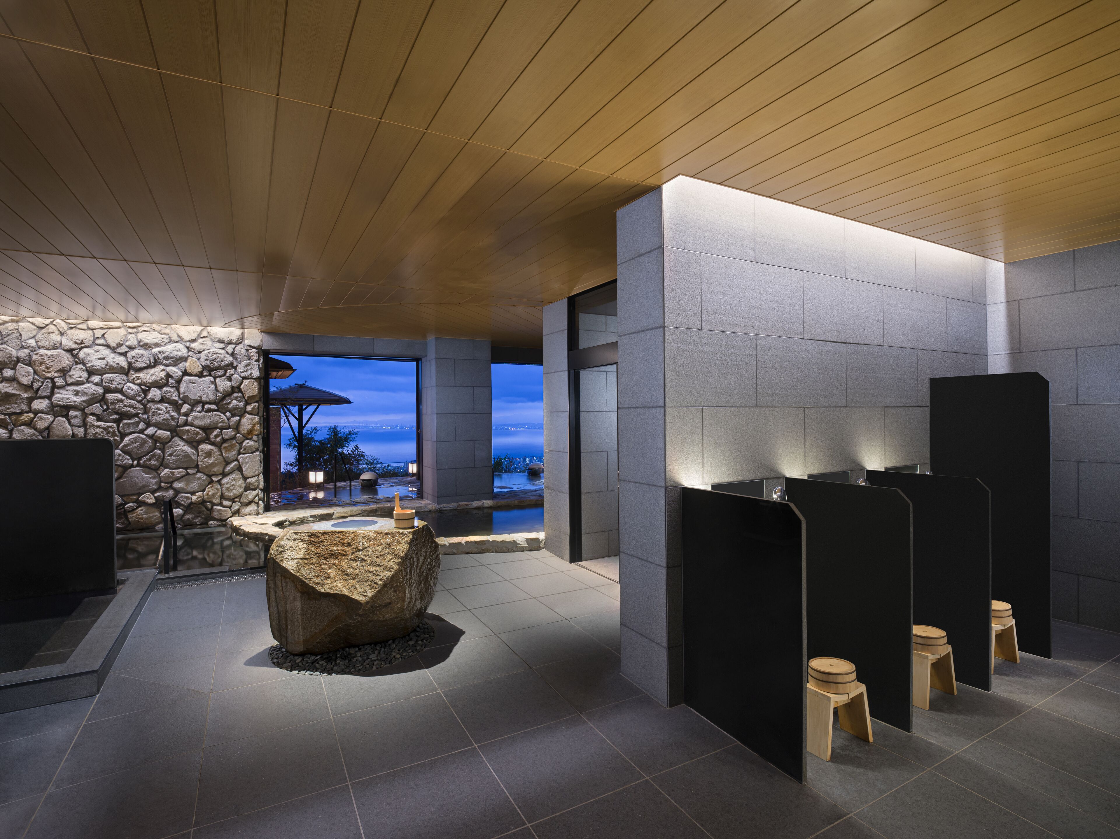 Une salle de bain moderne avec des murs en pierre, un plafond en bois et une vue sur l’eau.