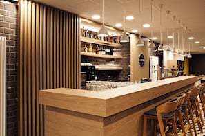 A bar area with a wooden counter, bar stools, and shelves stocked with bottles. - Holiday Inn Express Mulheim - Ruhr by IHG (Muelheim an der Ruhr)