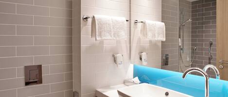 Un baño moderno con un lavamanos blanco, una cabina de ducha de vidrio y un espejo con dos toallas.