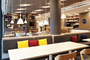 A modern cafe with seating arrangements, pendant lighting, and a bar area. - Holiday Inn Express Mulheim - Ruhr by IHG (Muelheim an der Ruhr)