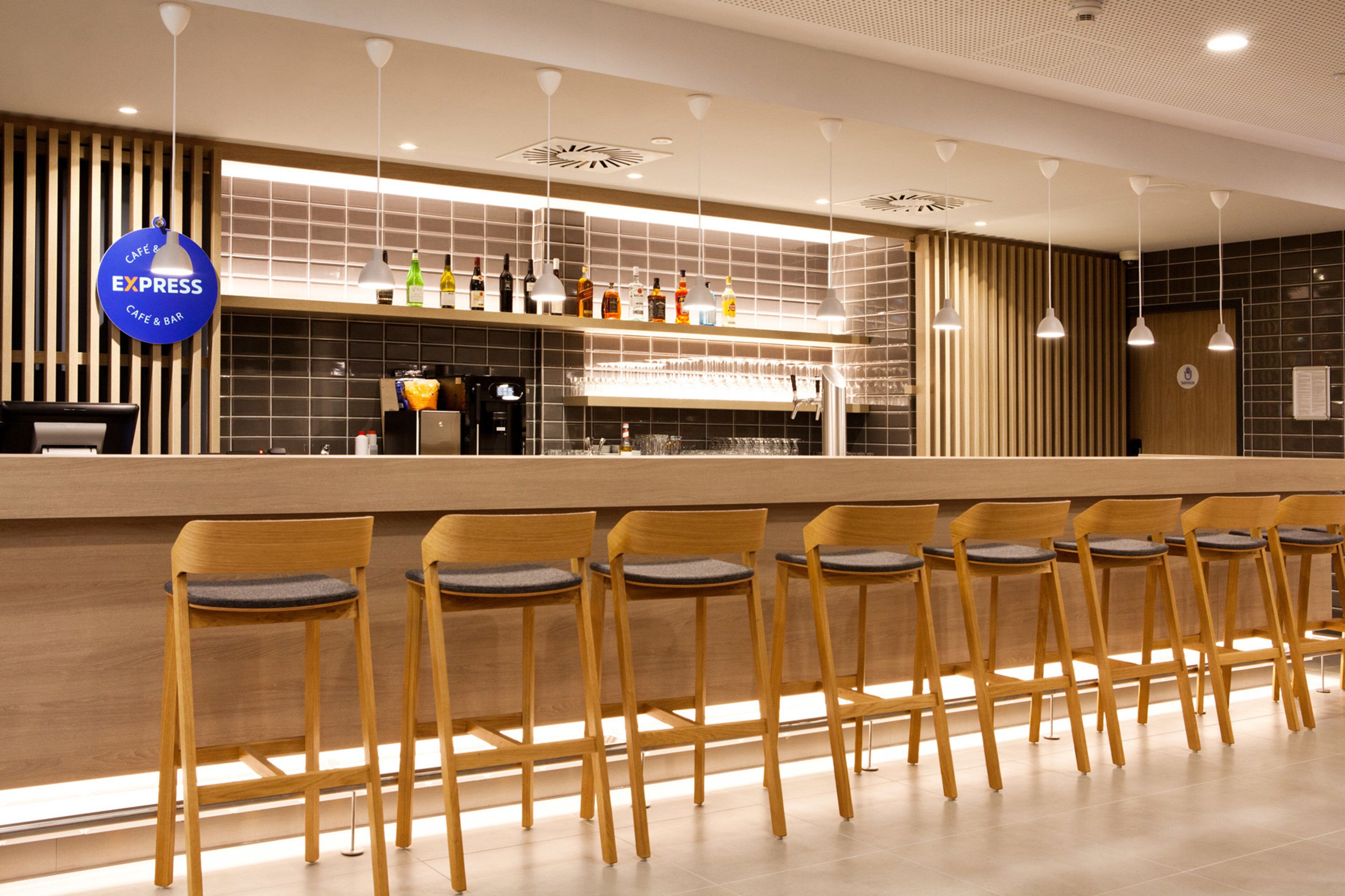 A modern bar area with a long counter, multiple bar stools, and a variety of bottles on the shelf.
