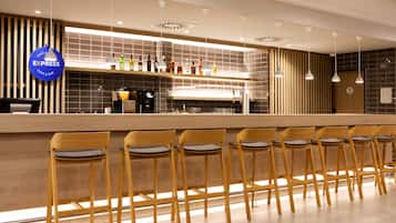 A modern bar area with a long counter, multiple bar stools, and a variety of bottles on the shelf.