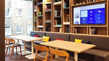 A modern library with bookshelves, a large digital display, seating area, and wooden tables.