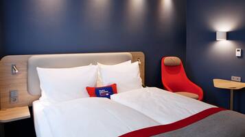 A modern hotel room with a large bed, a red chair, and a small table.