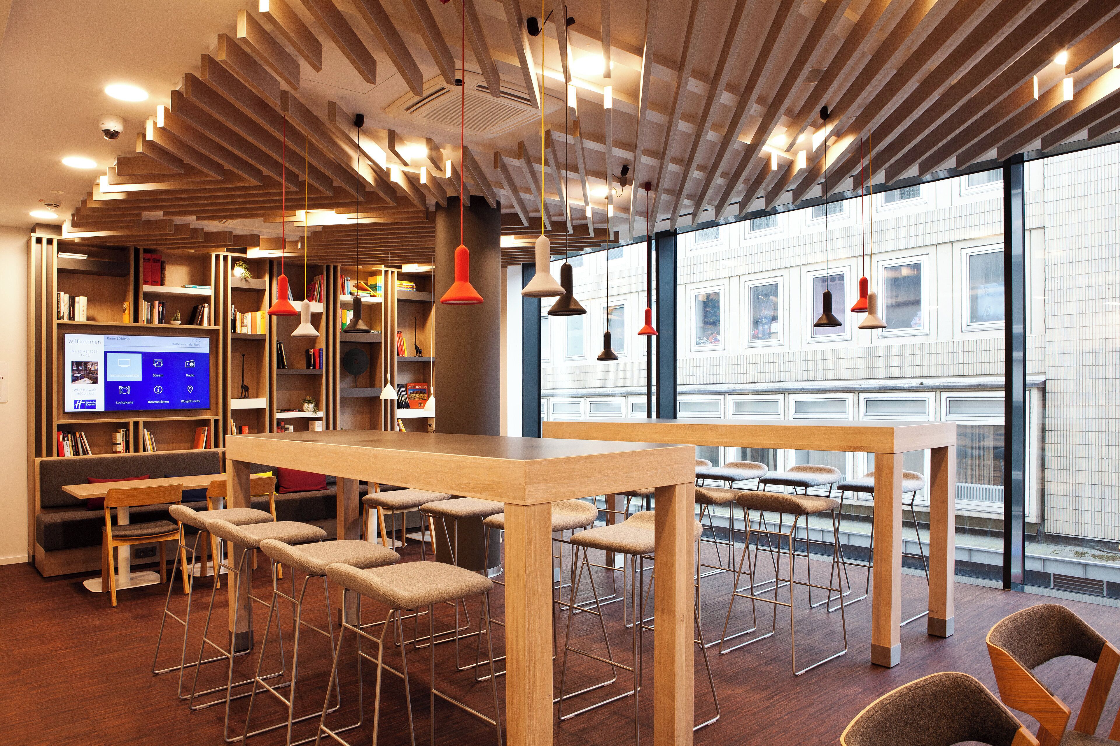 A modern interior with a long wooden table, bar stools, and bookshelves.