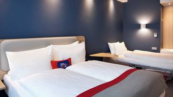 A hotel room with two beds, a bedside table, a wall-mounted light, and a thermostat.