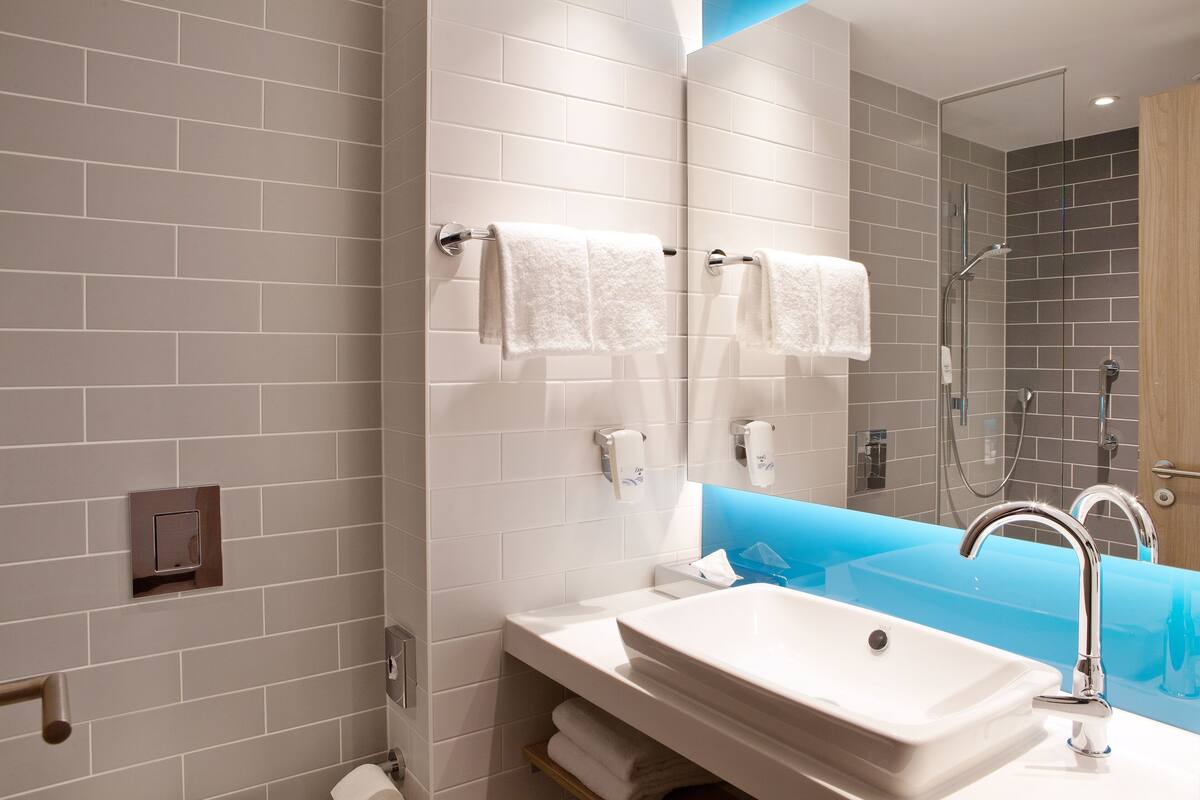 A modern bathroom with a white sink, a glass-enclosed shower, and a blue accent wall.