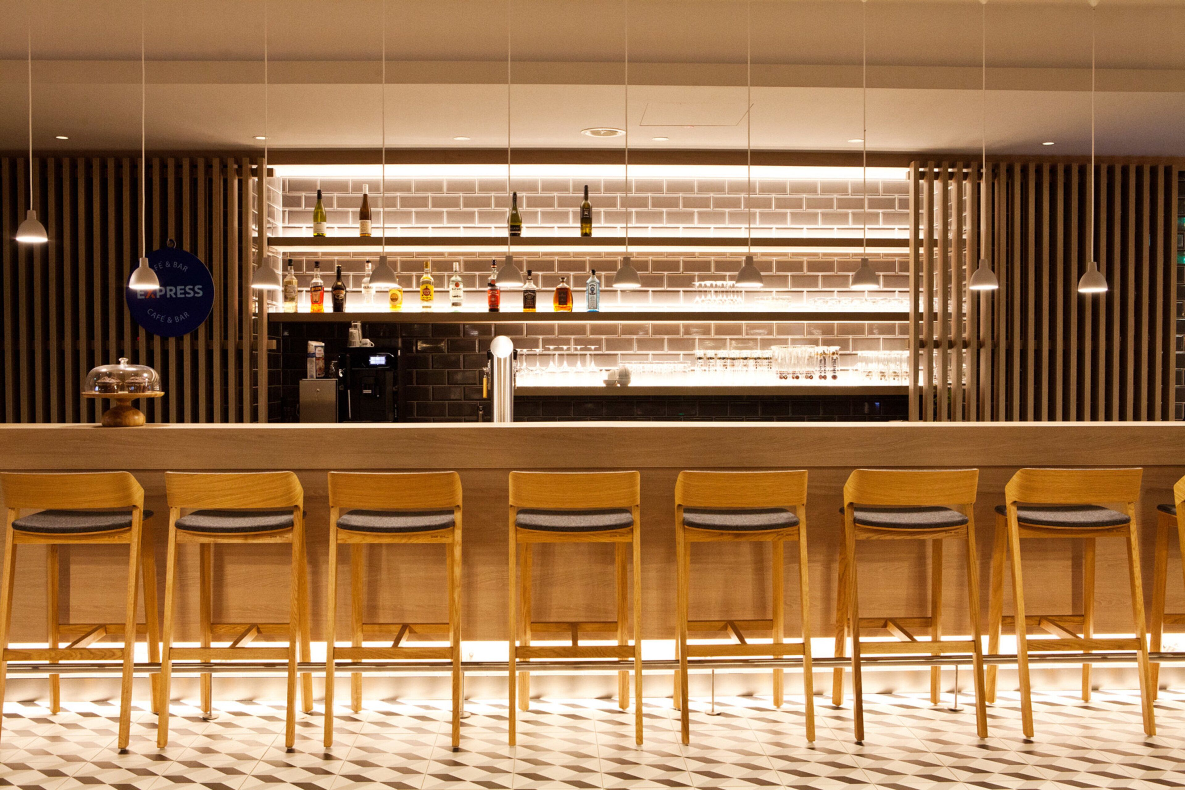 Un espace bar avec un comptoir, plusieurs étagères remplies de bouteilles et une rangée de chaises en bois.