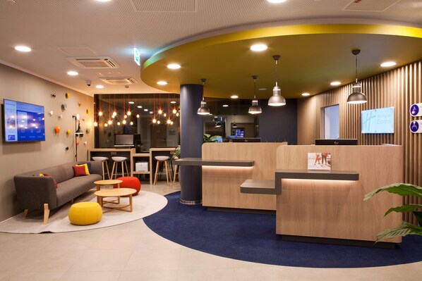 Un hall d’hôtel moderne doté d’un comptoir d’accueil, d’un espace salon et d’un téléviseur à écran plat.