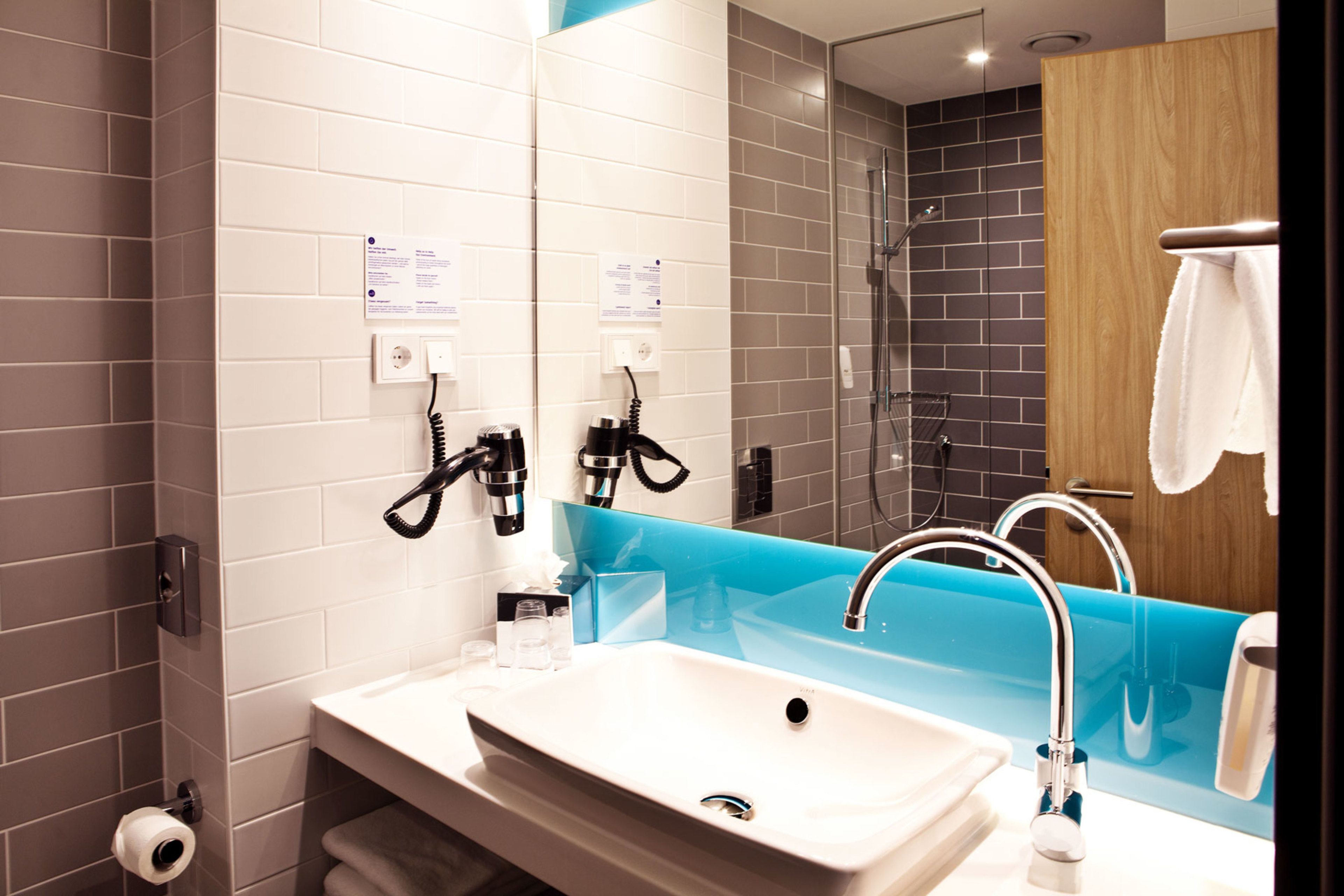Ein modernes Badezimmer mit einem weißen Waschbecken, einer blauen Akzentwand und einer Duschkabine aus Glas.