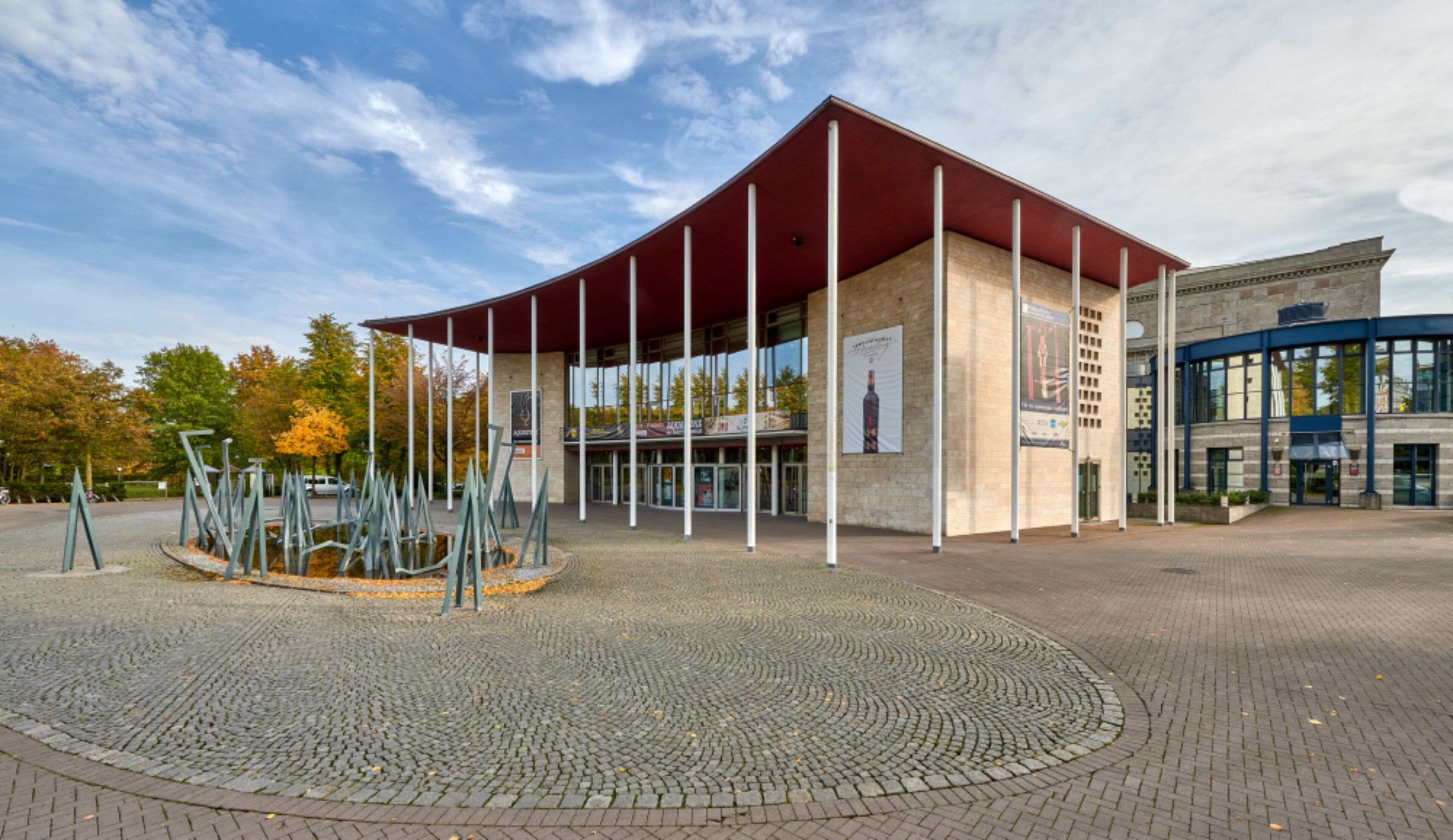Ein modernes Gebäude mit einer gewölbten Dachform und einem kreisförmigen Platz mit einer Skulptur.
