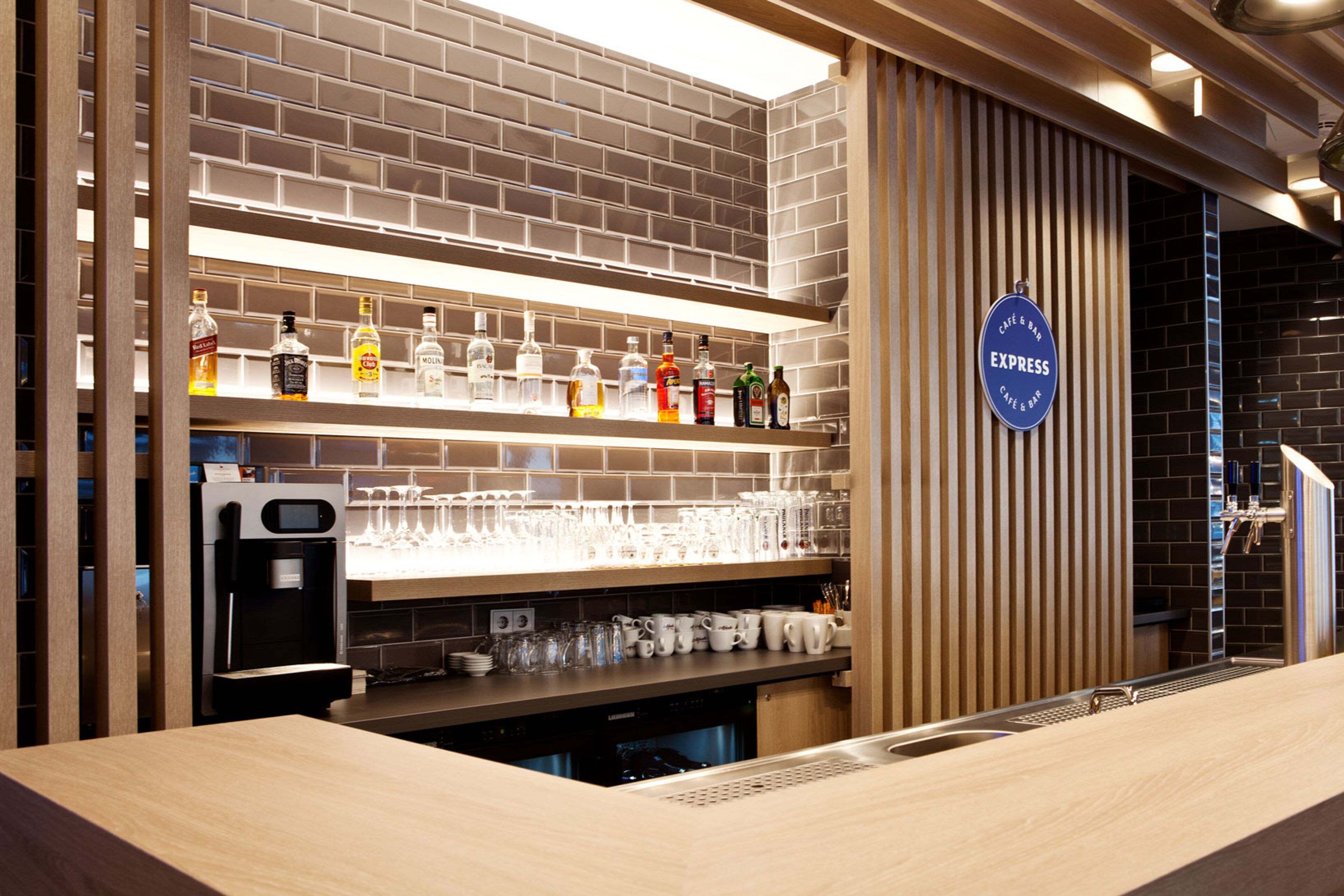 Uma área de bar com parede de tijolos, prateleiras com garrafas de bebidas e um letreiro que diz 'EXPRESS CAFE & BAR'.