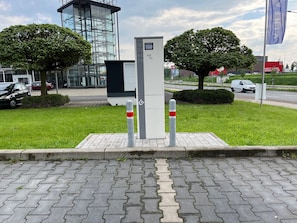 A modern building with a glass facade, a small kiosk, and a paved area with bollards.