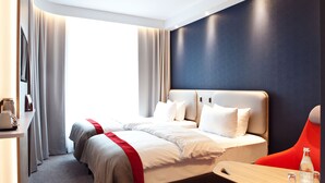 A hotel room with a large bed, a desk, and a chair. There is a window with curtains, a wall-mounted TV, and a bedside table with a lamp. - Holiday Inn Express Oberhausen by IHG (Oberhausen)