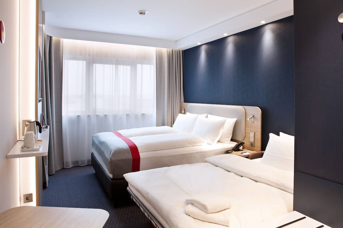A hotel room with two beds, a desk with a lamp, and a window with curtains.